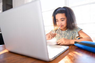 portrait of cute child doing homework on kitchen table with laptop