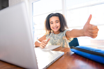 portrait of cute child doing homework on kitchen table with laptop