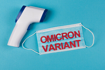 Top view of non-contact pyrometer near medical mask with omicron variant lettering on blue...