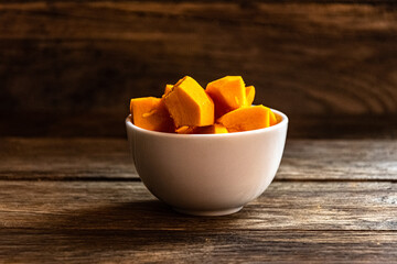 Sliced pumpkin in a white bowl on a wooden table.