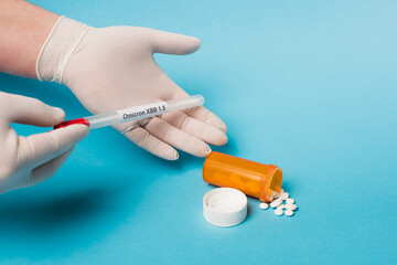 Cropped view of doctor in latex gloves holding throat swab with omicron lettering near pills on...