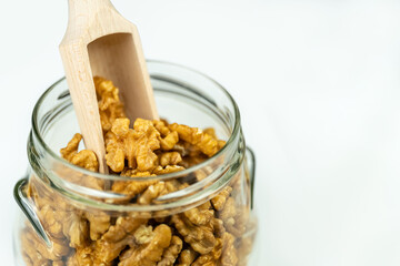 Glass jar full of peeled walnuts with wooden stick to catch them, isolated white background.