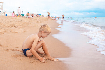 A blond boy playing on a tourist beach with sand. Summer fun vacation.