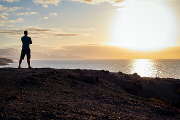 Man looks at the sea and the sunset on the coast of Fuerteventura in the evening light