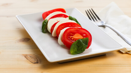 Fresh caprese salad over a white rectangular plate and a fork over a wooden table