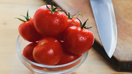Close up top view of tomatoes on a glass bowl and kitchen knife over a wooden table in front of a window