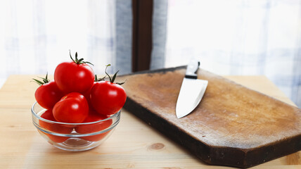 Tomatoes on a glass bowl and kitchen knife over a wooden table in front of a window