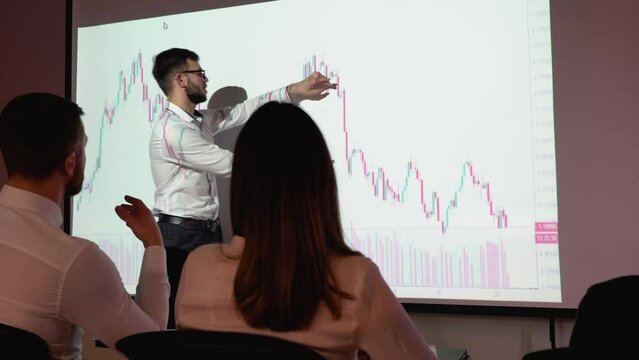 Young trader presents cryptocurrency investment strategy for group of investors. Wall TV showing big data analysis, infographics, stock market information, trends