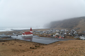 V&iacute;k &iacute; M&yacute;rdal Church above coastal Icelandic village on a foggy day wide shot