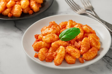 Plates with cooked POTATO GNOCCHI with tomato sauce on a white marble background. High angle view.