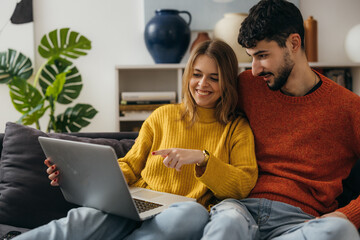 Woman sits on the sofa with her boyfriend and points finger at laptop