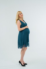 A beautiful pregnant woman in a turquoise dress hugs her stomach with her hands. Place for the text. White background.