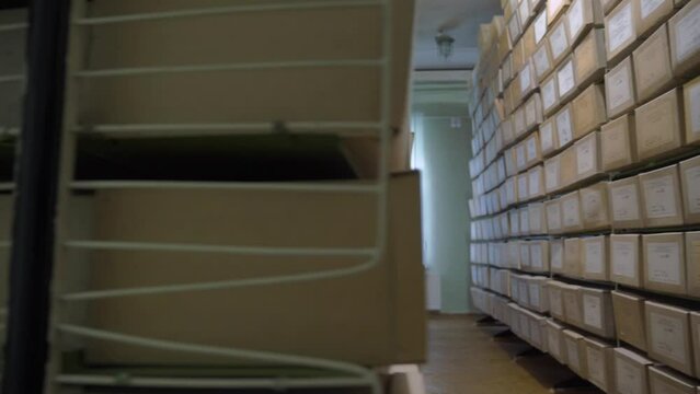 Archive storage with rows of metal racks keeping boxes on shelves and stepladders standing against windows illuminated by bright sunlight