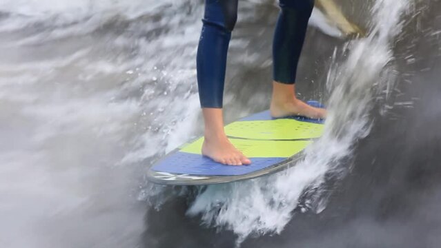 Man in dark swimming suit wakesurfs professionally picking up speed following motorboat on colorful board among waves in sea closeup