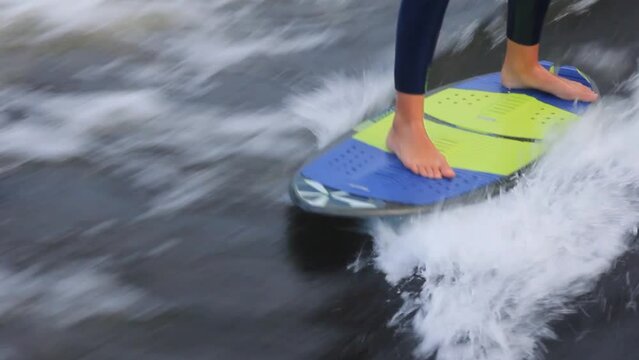Barefoot sportsman wearing neoprene swimsuit wakesurfs professionally at high speed standing on board among waves in sea closeup