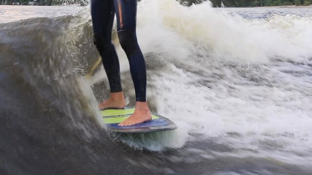 Barefoot man rider in blue swimming suit wakesurfs actively at high speed standing on colorful board among waves in sea closeup