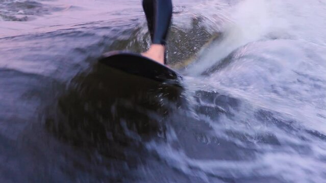Man in blue neoprene swimming suit performs stunts wakesurfing at high speed following boat on board among sea waves closeup