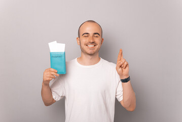 Cheerful balding man is full of hope while crossing fingers and holding passport.