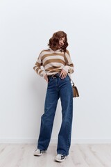 a full-length photo of a beautiful, stylish woman standing on a light background in a striped...