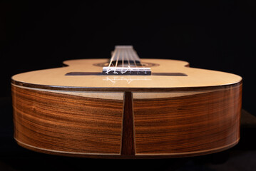 Classical guitar isolated on black background, view from the down side. Beautiful Brazilian wood -...