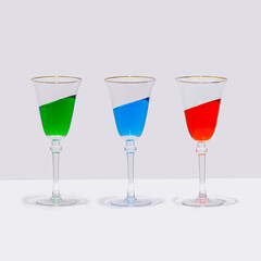 Three colorful cocktail glasses stand straight with the drink in them at an inclined angle. Surreal drinking culture, summer party or celebration composition.