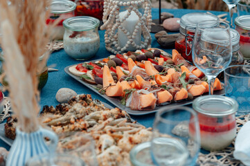Tasty food for outdoor summer picnic. Delicious appetizer, pieces of melon with jamon and tomatoes with mozzarella. Lunch on the beach by the sea.
