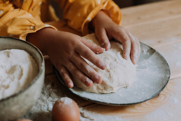 little girl in a yellow dress kneads dough from flour, eggs and water in the kitchen