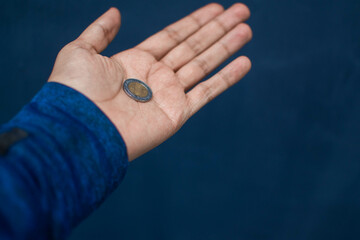 Mano sosteniendo una moneda de un peso mexicano sobre un fondo azul marino 