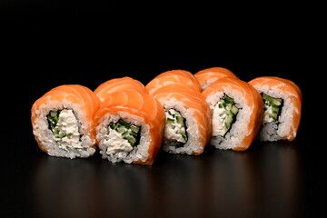 Close-up of Philadelphia sushi rolls with salmon, cucumber, avocado, cream cheese. On dark background.