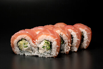 Close-up of tasty Philadelphia sushi rolls with salmon, cucumber, avocado, cream cheese. On dark background.