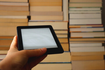 Hand holding e-reader in fornt of a pile of print books. Contemporary and traditional contrast. Selective focus.