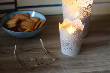 Glasses, bowl of biscuits, lit candles and books in the background. Selective focus.