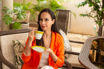 Uma jovem mulher tomando chá com expressão contemplativa, na varanda de sua casa. - obrazy, fototapety, plakaty