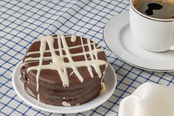Brown chocolate alfajor, typical candy in Argentina, with a cup of coffee on a checkered tablecloth.