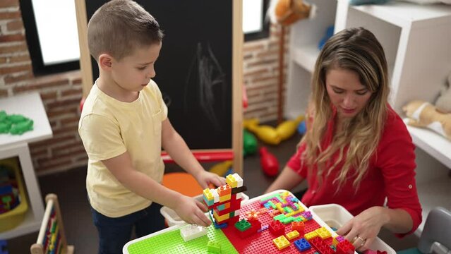 Teacher and toddler playing with construction blocks sitting on table at kindergarten