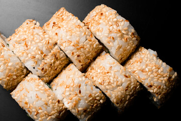 Close-up top view on sushi rolls california with decorated with sesame seeds on dark background.
