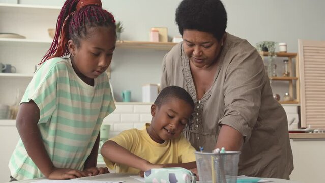 African American grandmother helping two tween grandchildren with their school homework, studying at kitchen table