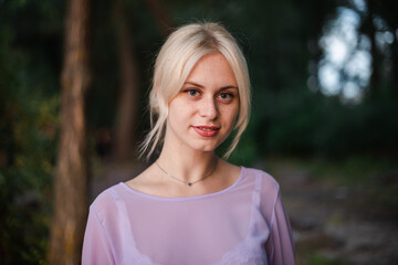 Fototapeta premium Blonde girl on a summer day on the shore near the river in nature in a dress