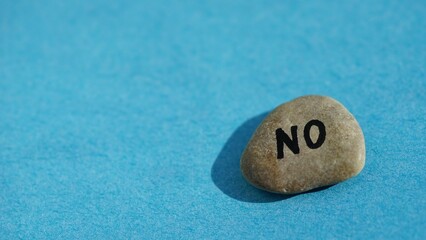 Obraz na płótnie Canvas Pebble stone with text no on it on blue sunny table