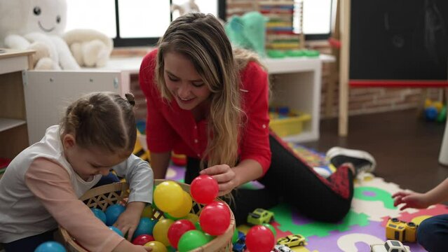 Teacher with boy and girl playing with balls sitting on floor at kindergarten