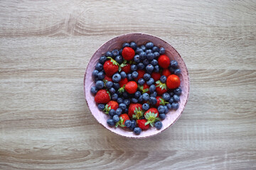 Pink rustic bowl filled with fresh blueberries and strawberries. Wooden background, top view.