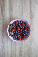 Pink rustic bowl filled with fresh blueberries and strawberries. Wooden background, top view.