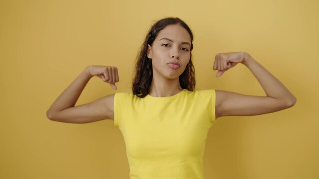 Young african american woman smiling confident doing strong gesture with arms over isolated yellow background