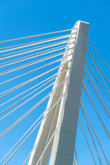 a side on image of a white concrete bridge pillar and cables against blue skies 