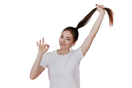 Cheerful Italian young woman in white t-shirt making ok sign , looking at camera, pulling ponytail up over transparent background. Pretty model, satisfied by hair. Healthy lifestyle, fitness, beauty.