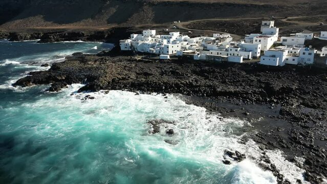 One of Lanzarote's less-known coastal towns, Tenesar is truly a beautiful little spot to appreciate Lanzarote's western coast - Drone arial view of white village houses and sae storm with waves surf 