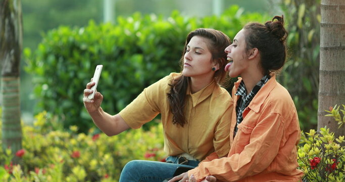 Two friends taking photo selfie with smartphone outdoors. Millennial young women posing to camera