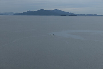 Small boat on the vast sea with far mountais in the background 