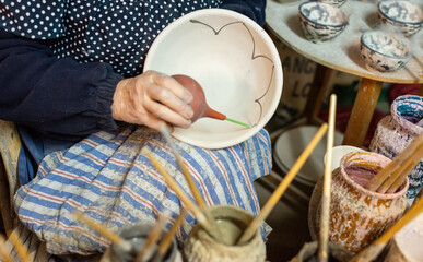 elderly craftswoman painting earthenware in her pottery workshop