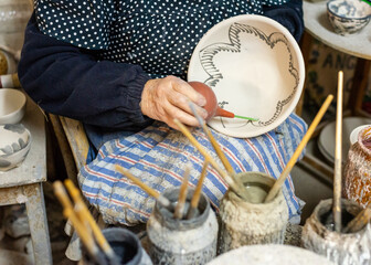 elderly craftswoman painting earthenware in her pottery workshop